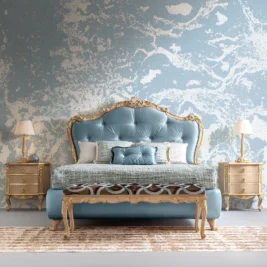 This bedroom exudes classic elegance with a blue and gold ornate bed and a Classic Style Ornate Bedside Cabinet. The textured blue and white abstract wall perfectly complements the decor, while a striped rug sits beneath a bench with a patterned cushion.
