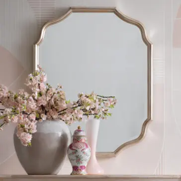 Curved Italian Wall Mirror A decorative Curved Italian Wall Mirror with an ornate, scalloped gold frame hangs above the mantel. On the mantel, there is a large beige vase filled with pink cherry blossoms, a decorative porcelain jar with a floral pattern, and a simple white and pink vase.