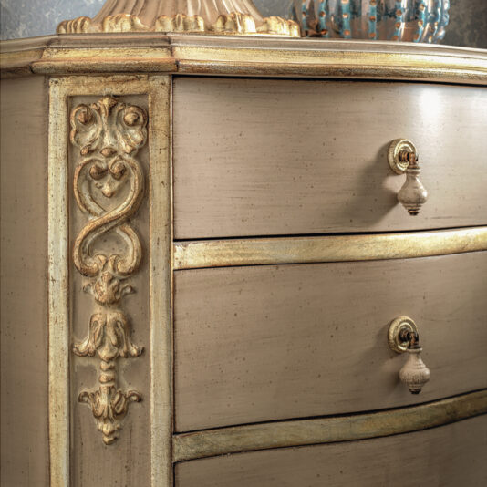A close-up of the Ornate Classic Style Chest Of Drawers reveals its elegantly antique design with intricate carvings and golden accents. This classic dresser boasts two rounded drawers with vintage handles, highlighting detailed craftsmanship and a harmonious blend of beige and gold tones.