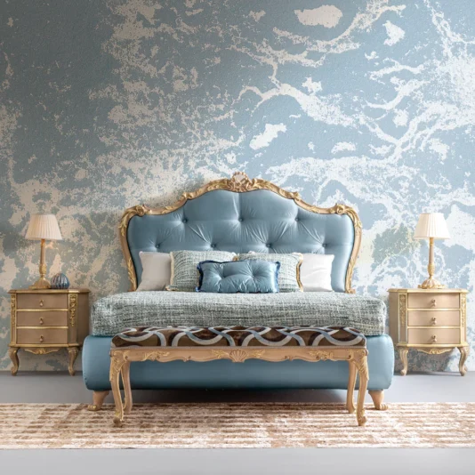 Ornate Rococo Style Bench A luxurious bedroom features an ornate blue and gold bed, two matching nightstands with lamps, and an Ornate Rococo Style Bench adding elegance. The abstract blue and gray wall pattern completes the look along with a patterned rug.