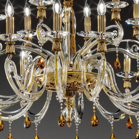 Candelabra Style Chandelier With Swarovski Crystals The Candelabra Style Chandelier With Swarovski Crystals, featuring multiple candle-style light bulbs and adorned with intricate golden and clear glass details, is illuminated against a dark background.