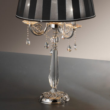 Candelabra Style Table Lamp With Swarovski Crystals The Candelabra Style Table Lamp With Swarovski Crystals boasts a silver base, a black striped lampshade, and features intricate metalwork adorned with hanging Swarovski crystal ornaments, perfectly combining elegance with a vintage vibe.