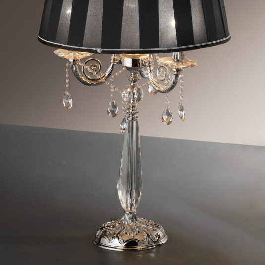 The Candelabra Style Table Lamp With Swarovski Crystals boasts a silver base, a black striped lampshade, and features intricate metalwork adorned with hanging Swarovski crystal ornaments, perfectly combining elegance with a vintage vibe.