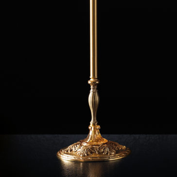 Classic Dimpled Amber Glass Floor Lamp A close-up of an ornate gold-colored lamp base set against a black background, showcasing intricate floral and leaf patterns with a slender, fluted stem extending upward. The design is reminiscent of the Classic Dimpled Amber Glass Floor Lamp. The reflective surface enhances the elegant details of the lamp.