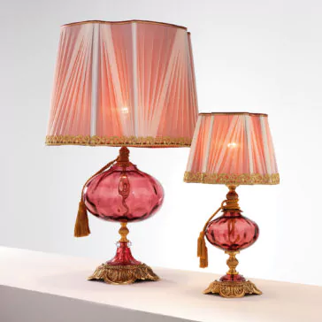 The Classic Dimpled Rose Glass Table Lamp features an elegant design with a dimpled rose glass base and a matching pleated red lampshade adorned with gold trim. Each lamp showcases intricate detailing with gold accents and decorative tassels hanging from the neck. The larger lamp is situated on the left, while a smaller one sits to the right.