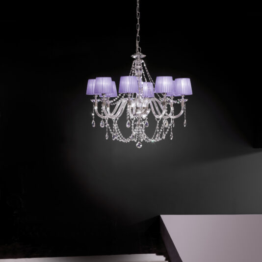 The Clear Glass Chandelier With Pleated Shades, adorned with hanging glass ornaments, is suspended from the ceiling against a dark background. This chandelier boasts multiple curved arms and intricate detailing, creating an elegant and sophisticated appearance.