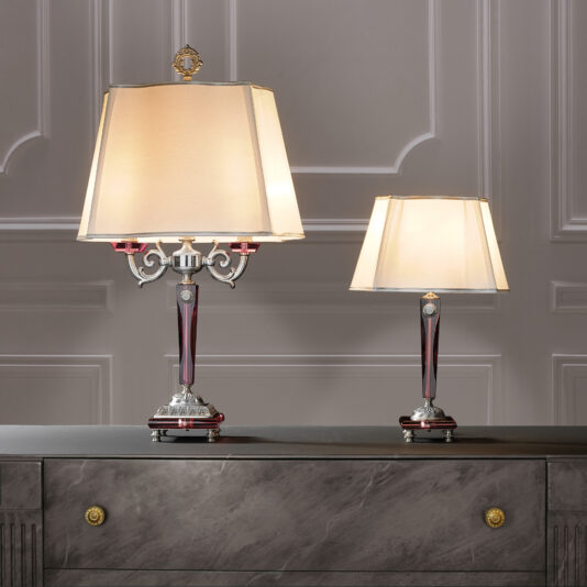 High End Antique Rose Glass Table Lamp Two elegant High End Antique Rose Glass Table Lamps with beige lampshades sit gracefully on a sleek gray chest of drawers with golden knobs. The lamps have intricately designed metallic bases with red accents, placed against a backdrop of a white paneled wall.