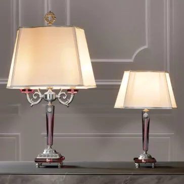 High End Antique Rose Glass Table Lamp A photo depicts two exquisite High End Antique Rose Glass Table Lamps with beige shades resting on a marble surface. The larger, luxurious lamp showcases an antique rose glass base adorned with red and silver accents and intricate detailing. The smaller lamp presents a more straightforward design while maintaining the same elegant color scheme. Both lamps are set against a refined grey wall, enhancing their sophisticated appeal.