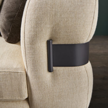 High End Contemporary Modular Corner Sofa Here's a rephrased version of the sentence using the given product data:
Close-up view of the back of the High End Contemporary Modular Corner Sofa, featuring beige upholstery with dark brown accents and a black, flat rectangular metal bracket attached to its side. The background showcases wooden flooring and a dark green wall.
