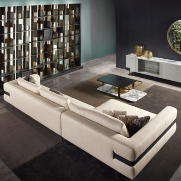 High End Contemporary Modular Corner Sofa A modern living room featuring a High End Contemporary Modular Corner Sofa, a dark wood coffee table, and a sleek entertainment unit. A decorative shelving unit spans the back wall, with a round mirror hanging above. The space is adorned with minimalist decor in neutral tones.