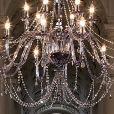 The Large Modern Smoked Glass Chandelier, adorned with numerous crystal beads and lit candles, hangs from an ornate, vaulted ceiling. This chandelier features multiple arms and cascading crystal strands, creating an elegant and luxurious ambiance.