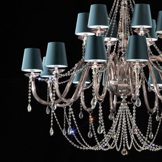 The Large Modern Smoked Glass Chandelier With Shades is an elegant, expansive lighting fixture boasting multiple branches adorned with crystal droplets and teal lampshades. Its intricate design features reflective surfaces and dangling crystals set against a black background, enhancing its luxurious appearance.
