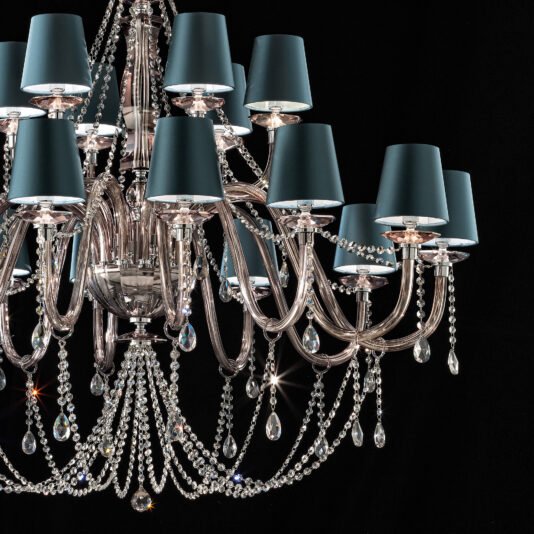 The Large Modern Smoked Glass Chandelier With Shades is an elegant fixture featuring multiple tiers of lights, each enveloped by teal blue lamp shades. This chandelier boasts ornate silver arms and is lavishly adorned with numerous crystal beads and smoked glass pendants, creating a luxurious and sparkling appearance against a dark background.