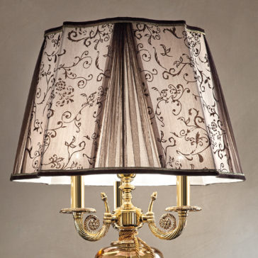 Large Ornate Amber Glass Table Lamp A close-up of the Large Ornate Amber Glass Table Lamp showcases its gold base with intricate scrollwork, complemented by a pleated lampshade adorned with elegant black floral patterns. The lampshade's design adds a touch of classic sophistication to the lamp's overall appearance.