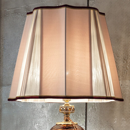 A close-up view of the Large Traditional Amber Glass Table Lamp showcases a classic lampshade with a muted pink color, gold trim, and a gold base. The pleated fabric creates a delicate, elegant look with subtle light and shadow details. This combination brings an air of timeless sophistication to any space.