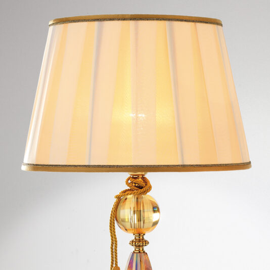 Luxury Amber Glass Table Lamp The Luxury Amber Glass Table Lamp features a beige pleated lampshade and an ornate base adorned with a spherical crystal accented in gold, complete with a golden rope tied around it. The background is set against a simple, light gray color.