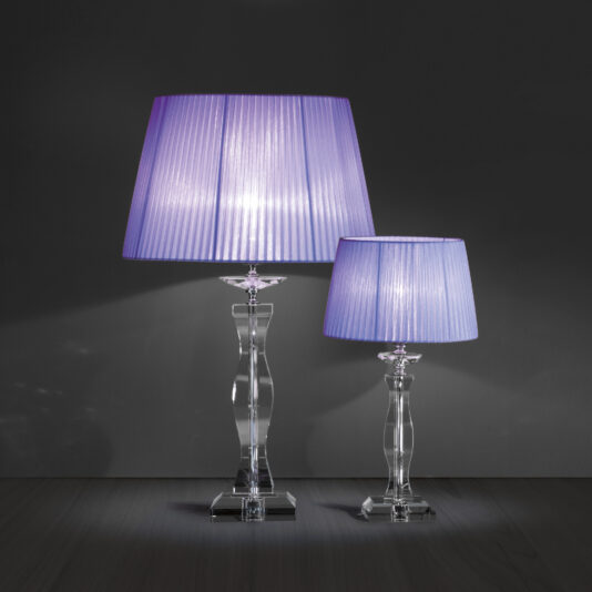 Two sleek **Modern Glass Table Lamps With Pleated Shades** are showcased against a dark background. These lamps feature transparent bases and pleated, lavender-hued shades that emit a gentle glow. The taller lamp is placed on the left, while the shorter one sits on the right.