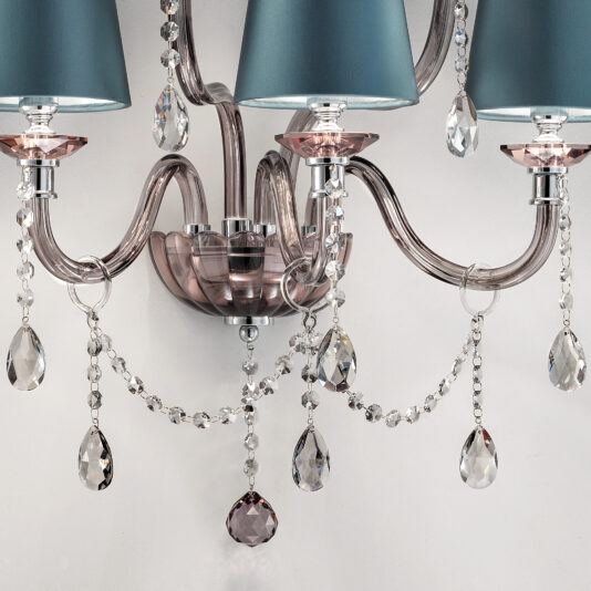 Modern Smoked Glass Wall Light With Shades A close-up of an elegant chandelier with turquoise drum shades showcases its clear, curved arms adorned with hanging crystal beads and pendants. This sophisticated design exudes the same luxurious appeal as the Modern Smoked Glass Wall Light With Shades, all set against a plain white background.