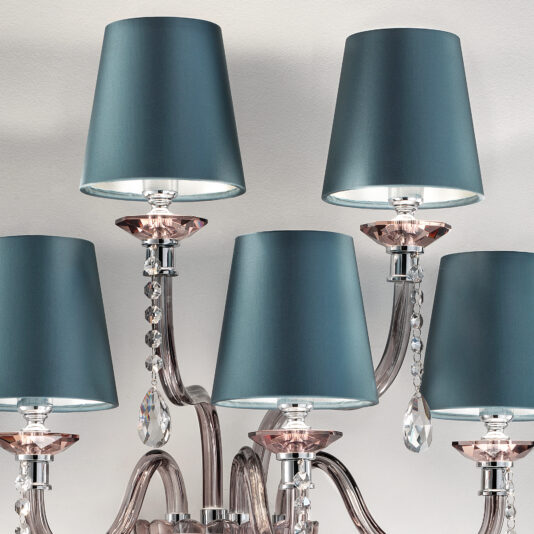 Modern Smoked Glass Wall Light With Shades A close-up of a stylish chandelier with five arms, featuring teal fabric lampshades and crystal accents. The chandelier has a polished metallic finish and elegant curves, reminiscent of the Modern Smoked Glass Wall Light With Shades, with crystal droplets hanging below each lampshade.