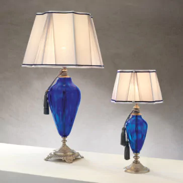 Traditional Style Dimpled Blue Glass Table Lamp Two Traditional Style Dimpled Blue Glass Table Lamps, featuring elegant blue bases with subtle dimples, white lamp shades with blue trim, and hanging tassels for a touch of sophistication. The larger lamp is positioned on the left and the smaller one on the right, both set against a neutral gray background.