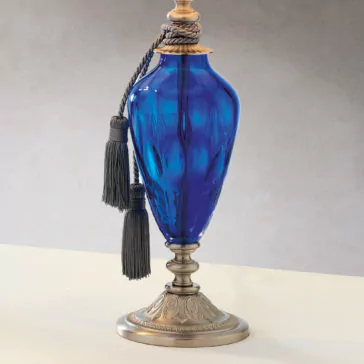 Traditional Style Dimpled Blue Glass Table Lamp A decorative traditional-style table lamp with a dimpled blue glass body and a metallic base and top, featuring ornate designs. The lamp is adorned with a gray rope tied around the neck, ending in two tassels that hang along its side. Set against a plain, light-colored surface, this elegant piece resembles an intricate vase.