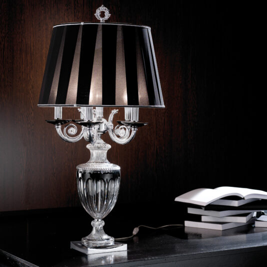 An elegant Candelabra Style Large Glass Table Lamp with a black and white striped shade sits on a dark wooden surface. The lamp features intricate detailing on its glass base. An open book and two closed books are nearby, adding to the sophisticated ambiance of the scene.