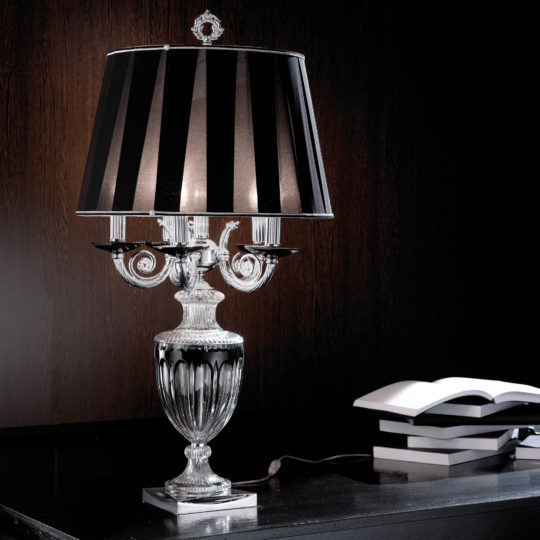 An elegant Candelabra Style Large Glass Table Lamp with a black and white striped shade sits on a dark wooden surface. The lamp features intricate detailing on its glass base. An open book and two closed books are nearby, adding to the sophisticated ambiance of the scene.