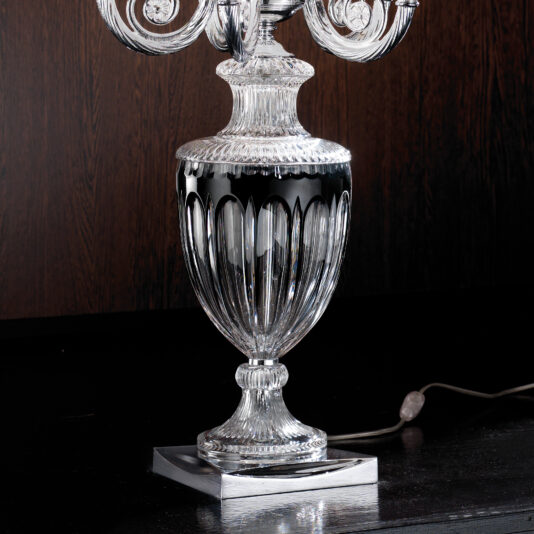 Candelabra Style Large Glass Table Lamp A close-up image showcases the Candelabra Style Large Glass Table Lamp, featuring an elegant, transparent base with intricate patterns and a sophisticated candelabra design, placed on a dark wooden surface. The power cord of the large table lamp is visible, trailing from the back.