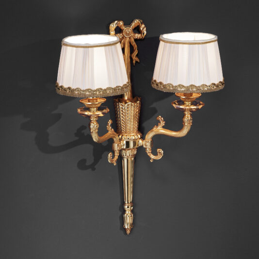 Classic Style French Gold Double Wall Light The Classic Style French Gold Double Wall Light, adorned with intricate detailing and two white fabric shades, is mounted against a dark background. The sconce showcases elegant curved arms and decorative designs, exuding a vintage and luxurious appearance.