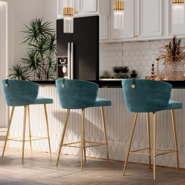 A contemporary kitchen showcases three Contemporary Teal Velvet Bar Stools with gold legs along a black counter, enhanced by plants, glass pendant lights, and a hexagonal tiled backsplash. A double-door fridge stands in the background.