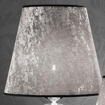 A grayscale close-up photo of a lamp with a textured lampshade. The velvety material of the lampshade showcases an elegant mottled pattern, mirroring the sophistication of a Glamorous Swarovski® Crystal And Pearl Table Lamp. The lamp is set against a plain, dark wall background.