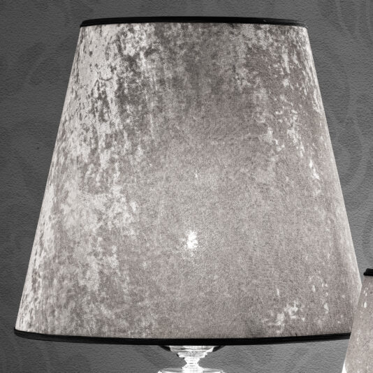 A grayscale close-up photo of a lamp with a textured lampshade. The velvety material of the lampshade showcases an elegant mottled pattern, mirroring the sophistication of a Glamorous Swarovski® Crystal And Pearl Table Lamp. The lamp is set against a plain, dark wall background.