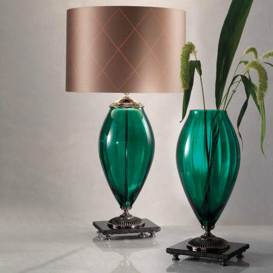 This decorative setup features the Green Glass Table Lamp and Vase With Rhinestones. The lamp boasts a beige lampshade adorned with subtle diamond patterns and rhinestones, while the matching green glass vase holds tall green leaves and ornamental grass. The entire arrangement is beautifully set against a light gray background.