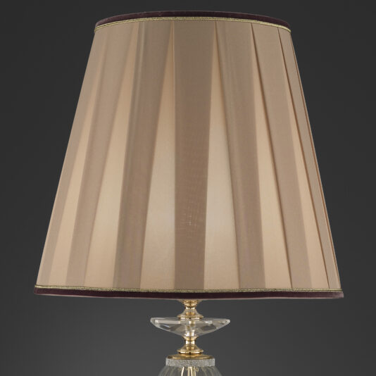 Large Table Lamp With Swarovski® Crystals The Large Table Lamp With Swarovski® Crystals features a tall, cylindrical beige fabric lampshade with vertical pleats, accented by thin dark brown trim at the top and bottom edges. The brass base is embellished with Swarovski® crystals, providing an elegant touch against the dark gray background.