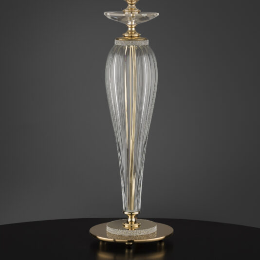 Large Table Lamp With Swarovski® Crystals A tall, elegant large table lamp with Swarovski® crystals and gold base and accents stands on a dark surface. Reminiscent of a ribbed glass vase with a narrow neck, the lamp features intricate details topped with a decorative glass stopper. The background is plain and dark, highlighting the lamp's sophisticated design.