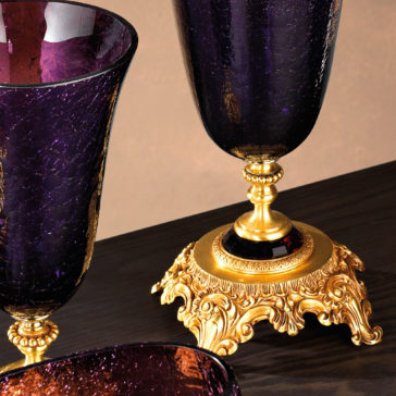 Luxury Amethyst Glass Vase And Bowl A close-up of the Luxury Amethyst Glass Vase and Bowl featuring intricate gold bases set on a dark wooden surface. The glass has a cracked appearance, and the gold bases are elaborately detailed with decorative designs.