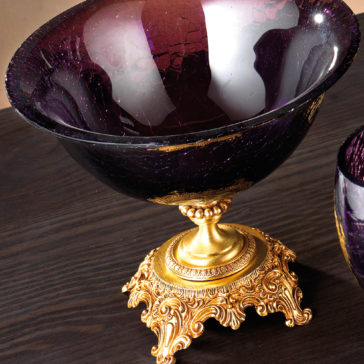 Luxury Amethyst Glass Vase And Bowl A close-up of the Luxury Amethyst Glass Vase And Bowl, highlighting its cracked texture, elegantly set on an intricately designed gold pedestal adorned with detailed swirling carvings and decorative embellishments, all beautifully resting on a dark wooden surface.
