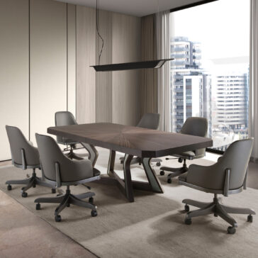 Luxury Veneered Boardroom Table A modern conference room featuring the Luxury Veneered Boardroom Table, accompanied by six gray swivel chairs and illuminated by a sleek black linear pendant light overhead. Large windows in the background provide a view of high-rise buildings. The room boasts beige walls and a partially carpeted floor.