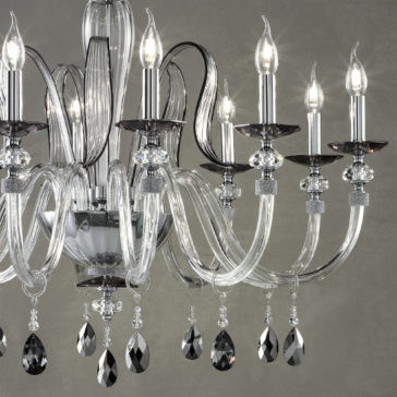 The Modern Chandelier With Swarovski® Crystals is a luxurious and ornate lighting fixture that boasts multiple candle-style lights, curved crystal arms, and hanging black and clear pendants. Against the plain grey background, it exudes an elegant and sophisticated appearance.