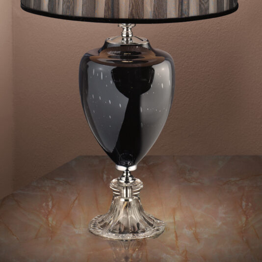 Modern Glass Table Lamp A sleek Modern Glass Table Lamp with a shiny black base and a fluted crystal stem stands on a marbled surface. The lampshade is striped in shades of brown and black, complementing the sophisticated design of the lamp.