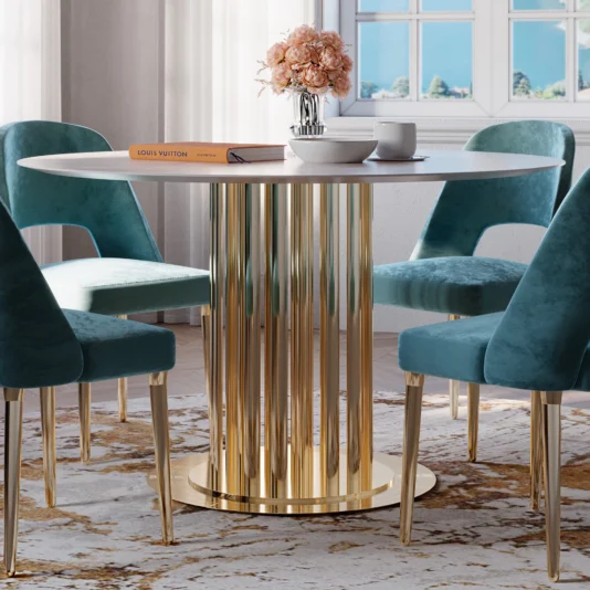 A dining room includes the Modern Round Marble Dining Table with a gold fluted base, complemented by four teal velvet chairs. A book and vase with flowers rest on the table, while sunlight from a nearby window illuminates the patterned rug.