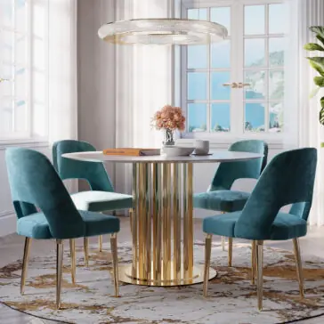 A stylish dining room showcases a Modern Round Marble Dining Table with a striking gold base, accompanied by four elegant blue velvet chairs and illuminated by a contemporary chandelier. At the center of the table, you'll find a vase filled with flowers and an open book. The room's ambiance is enhanced by its white walls and large windows that provide a scenic view, while a patterned rug adds a touch of texture to the space.