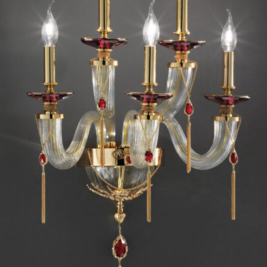 Swarovski® Crystal Candle Style Wall Light The Swarovski® Crystal Candle Style Wall Light is a sophisticated wall-mounted candelabra featuring five candle-shaped bulbs. This fixture combines gold and clear glass elements, embellished with Swarovski® crystals. The elegantly curved gold arms create an opulent and classic aesthetic in this exquisite candle-style wall light.