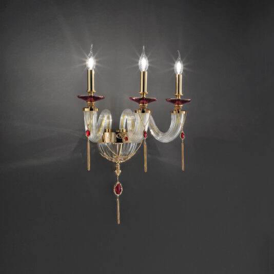 Triple Candle Style Wall Light With Swarovski® Crystals The Triple Candle Style Wall Light With Swarovski® Crystals is a stunning gold and glass wall-mounted chandelier, elegantly designed with three candle-shaped light bulbs adorned with red accents and clear glass curves. Its Swarovski® crystal ornamentation makes it stand out beautifully against a dark background.