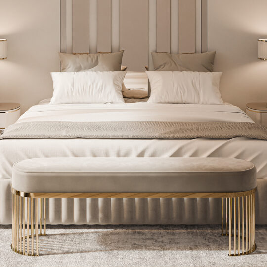 In a luxurious bedroom, a Contemporary Art Deco Style Bench with gold metal legs enhances the foot of a large bed adorned with white pillows and beige bedding. Symmetrical bedside tables and lamps complement the setup, while soft lighting adds coziness.