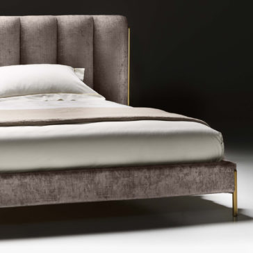 A close-up of the Contemporary Bed With Wide Headboard, featuring a beige upholstered headboard and frame. The bed is neatly made with white sheets and a beige top blanket, set against a dark, minimalist background.