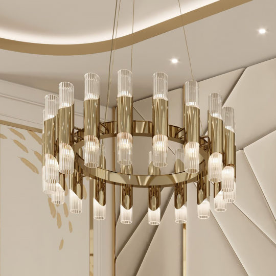 A Contemporary Chandelier With Engraved Glass Flutes, featuring vertical cylindrical glass lights hanging from a circular gold frame, is mounted on a modern, elegant ceiling adorned with sleek, curving lines and subtle geometric patterns in the background.