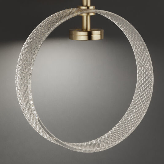 Contemporary Glass Ring Chandelier The Contemporary Glass Ring Chandelier features a textured, translucent circular design suspended from a brass fitting. This modern hanging light fixture emits a soft glow, accentuating the intricate patterns of the circular element against a dark gray background.