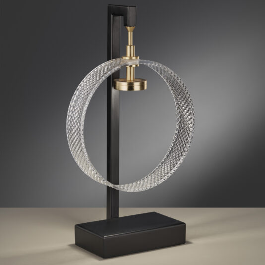 The Contemporary Glass Table Lamp showcases a unique design with a textured metallic ring suspended from a vertical black stand. This modern piece exudes a sleek, minimalist aesthetic featuring a golden bulb holder at the top center of the ring, all elegantly positioned on a black rectangular base.