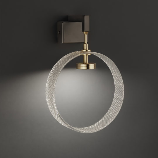 Mounted on a dark background, the Contemporary Glass Wall Light showcases a sleek, circular design. It features a brass-colored fixture paired with a textured glass ring that emits soft, diffused light, casting an elegant glow around the surrounding area.